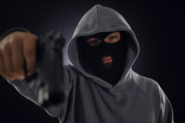 Criminal in mask with gun on dark background, selective focus
