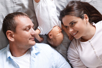 Fototapeta premium Mother and father with their newborn baby lying on bed at home, top view