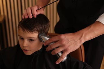 Professional barber working with little boy in barbershop, closeup