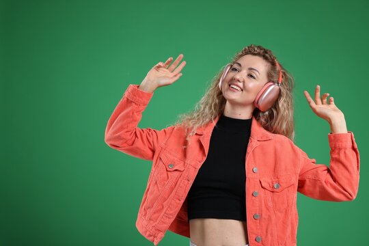 Happy woman listening to music in headphones and dancing on green background. Space for text - Powered by Adobe