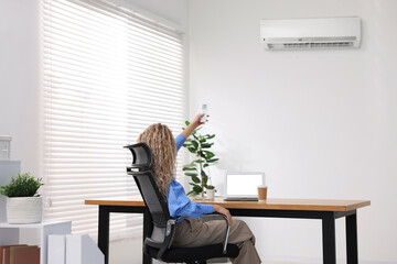 Woman using remote to control air conditioner in office