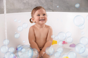 Cute little baby taking bath at home. Soap bubbles in air