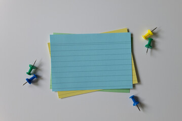Top view of blank index cards and push pins on a white background. A stack of colorful empty note...