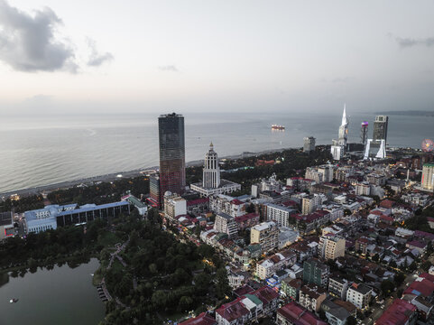 Aerial view of the sun setting over the Black Sea, casting a soft glow on the skyline with the Alphabetic Tower and Batumi Tower standing tall, Batumi, Adjara, Georgia.