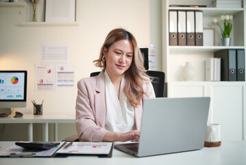 Naklejka premium Asian businesswoman working on laptop at modern office desk, smiling while checking emails.