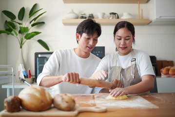Smiling couple rolling dough together in a bright kitchen during a fun baking session.