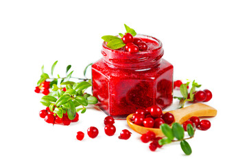 Jar of lingonberry jam with berries, leaves and wooden spoon isolated on white background.