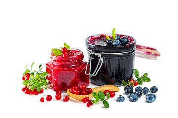 Jars of blueberry and lingonberry jam with berries, leaves and wooden spoon isolated on white.
