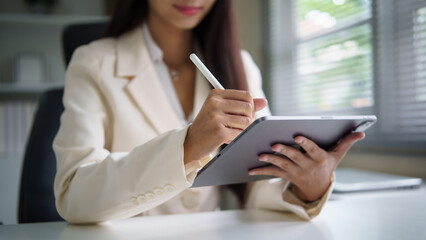  Close up of businesswoman in a white blazer holding a tablet and taking notes with a digital pen.