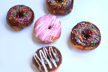Delicious Donuts with Chocolate, Pink, and Nut Toppings on White Surface.