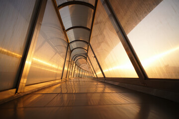 Obraz premium Illuminated walkway tunnel with transparent walls and ceiling at sunset creating a golden glow effect