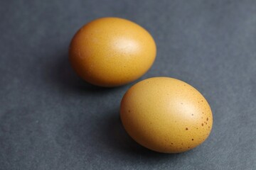 Two brown chicken eggs are placed on a dark surface, highlighting the natural texture of the shell...