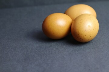 Three brown chicken eggs are laid on a dark surface, highlighting the shell's natural texture and...