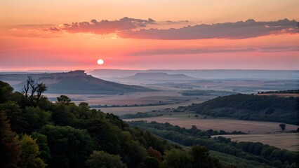 Serene Sunset over Rolling Hills: A breathtaking view of rolling hills and a distant mountain range unfolds as the sun sets, painting the sky with hues of orange and pink. 