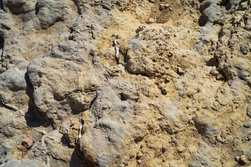 A detailed close-up of a rough, weathered rock and stone surface, creating a natural abstract background texture in sunlight.