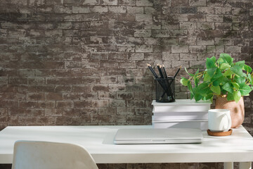 Minimalist desk with laptop, white coffee mug, potted plant, and stationery against a rustic brick wall background.