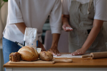Assorted loaves of homemade bread on a wooden board with a blurred couple working in the background.