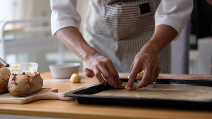 Close-up of hands placing rolled cookie dough onto a baking tray in a cozy kitchen setting.