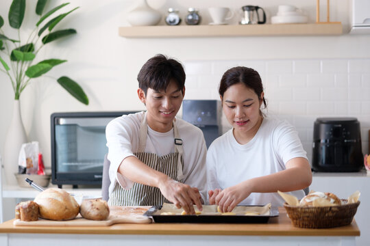 Young couple preparing cookies together in a bright modern kitchen, placing dough on a baking tray.