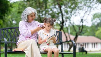 A loving grandmother gently supports her granddaughter as she focuses on drawing in a sketchbook.