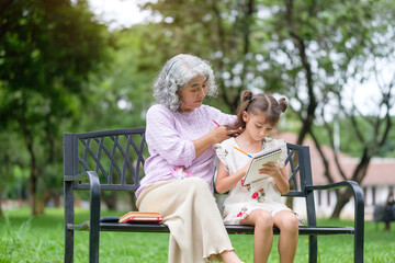 Tender moment of care and creativity between a senior woman and young girl on a park bench.