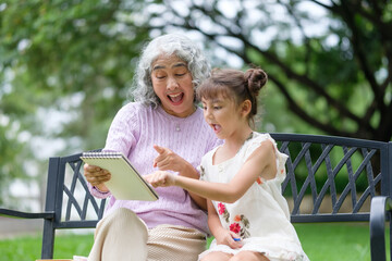 Cheerful grandmother and granddaughter drawing together in a sketchbook on a park bench.