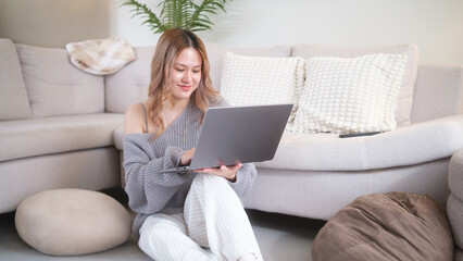Woman sitting on the floor using a laptop in a bright, cozy living room.