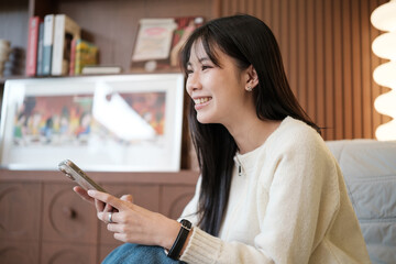 Young woman smiling while using a smartphone indoors in a cozy room.