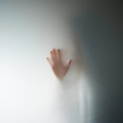 A blurry image of a hand pressing against a frosted glass or similar translucent material surface