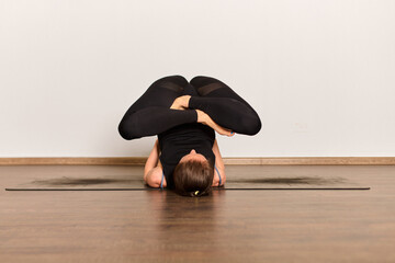 Practitioner in complex yoga pose on wooden floor, surrounded by minimalistic white walls. Soft...