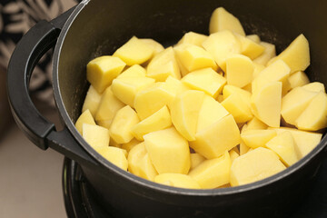 Fresh peeled potatoes in black pot. Raw potato pieces prepared for cooking. Homemade food...