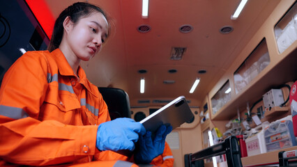 Asian woman emergency medical technician (EMT) or paramedic nurse using tablet in ambulance car