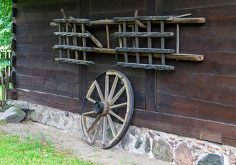 Wooden farming tools and wagon wheel hung on the cottage wall, traditional element of rural...