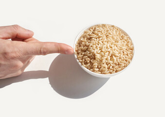 Caucasian hand pointing at bowl of brown rice on white background with shadow.