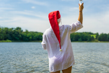  A girl with their back to the camera, wearing a white shirt and a santa hat, raises a glass of...