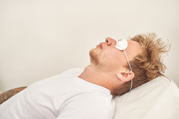Young caucasian male relaxing with protective eyewear on comfortable pillow in bright room.