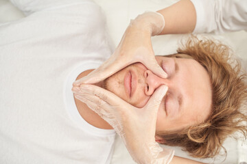 Facial massage therapy for relaxation on caucasian male adult with gloved hands on face.