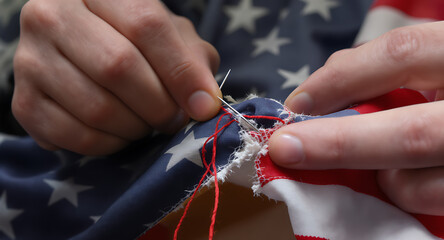 Hands sewing a torn American flag with needle and red thread, symbolizing patriotism, repair, and resilience.