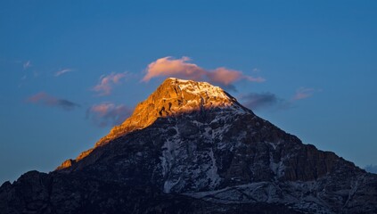 Majestic snow-capped mountain peak glows with golden sunlight against a clear blue sky at sunrise