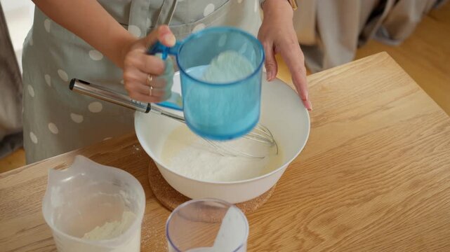Sifting flour through a sieve directly into a bowl with batter to make it airy. A woman prepares the dough for a homemade cake or pancakes, carefully adding the dry ingredient to the mix.