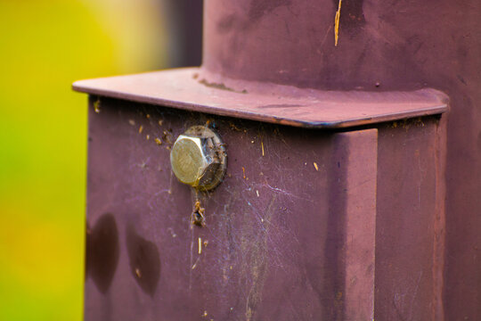 A close-up of a weathered steel beam with a bolt, faint rust, and cobwebs, blending industrial grit with organic detail against a blurred background.