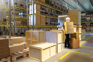 Industrial warehouse. Man carrying boxes in storage. Loader working inside warehouse hangar. Guy with boxes in hangar with distribution center. Warehouse interior with pallet racks