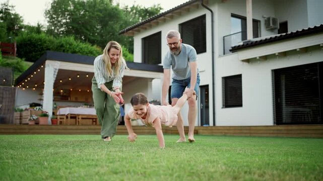 Parents playing wheelbarrow game with daughter in backyard.