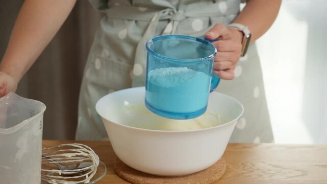 Culinary tutorial on making perfect batter. A housewife adds sifted flour to the wet ingredients and whisks the dough for a homemade cake, following a traditional family recipe.