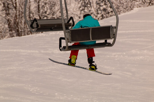 A snowboarder in bright gear rides a ski lift over a snowy mountain slope, heading up for the next ride on a winter day.