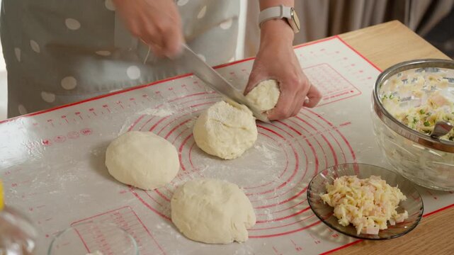 A woman preparing food in batches by shaping dough into small balls. Meal prep concept for making ahead homemade dumplings, pies, or buns with a savory filling.