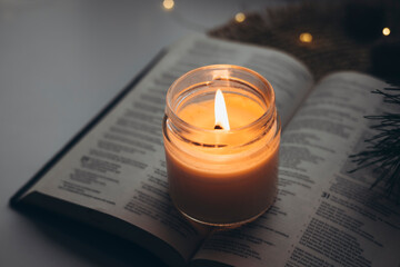 Burning candle and open Bible book with bokeh garland lights, Christmas background. Concept for...