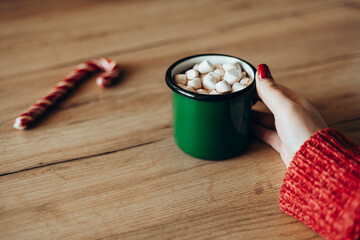 A cup of cocoa with marshmallows in the hand of a woman in a red sweater. Christmas background with...