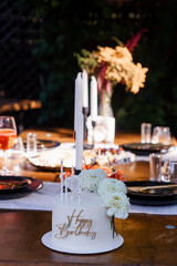 Intimate Birthday Celebration Scene with White Cake, Candles, Floral Arrangement and Warm Lighting...