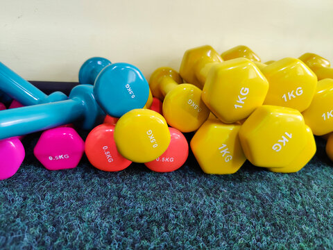 Various rubber-coated dumbbells stacked on a gray carpet. Gym equipment laid out on floor. Different colors, shapes, weights. For sports training. Copy space for text.